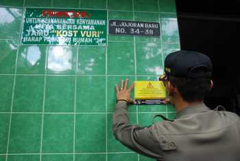 Petugas menempelkan stiker imbauan warga luar Kota Surabaya wajib mengurus SKTS di dinding salah satu rumah kos di Jojoran Baru saat operasi yustisi, Selasa (12/7) kemarin. [Gegeh Bagus/bhirawa] 