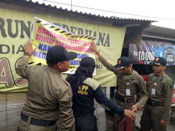 Anggota satpol PP kota Mojokerto memasang tulisan peringatan ancaman pembongkaran warung yang diduga dijadikan tempat prostitusi terselubung. (kariyadi/bhirawa)